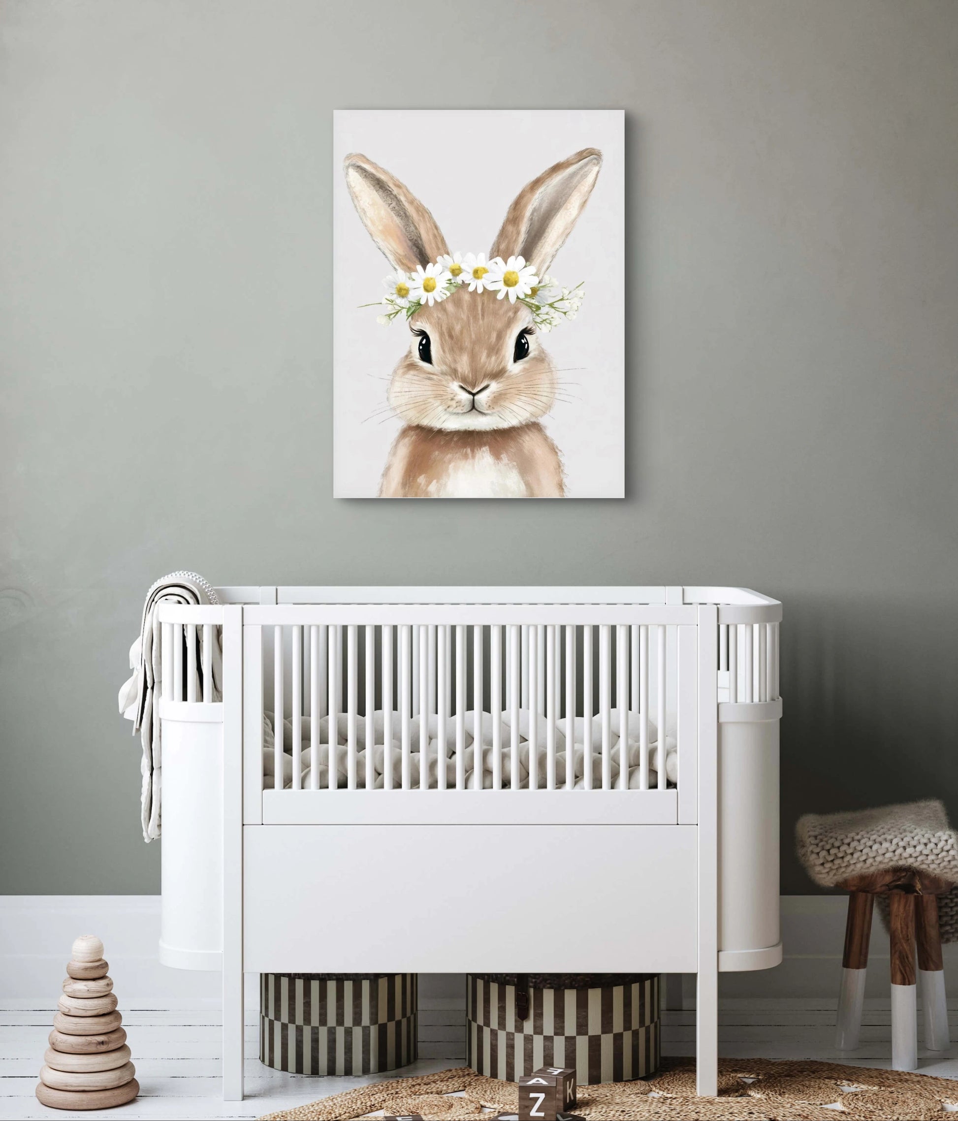 Kunstwerk van konijn met bloemenkrans boven een wit babybedje in neutrale kinderkamer met grijze muur