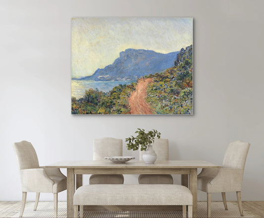 Kunstwerk “La Route de la Corniche, Cap d’Antibes” boven een lichte houten eettafel in een rustig, elegant interieur
