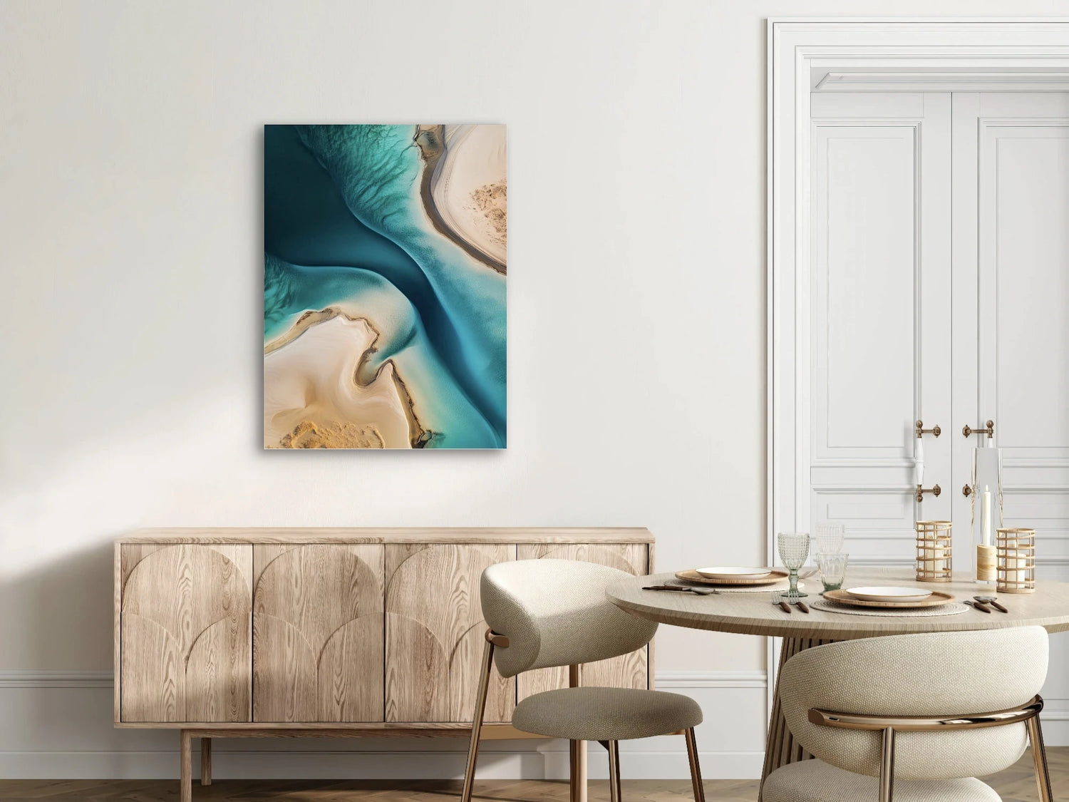 Textielkunstwerk met luchtfoto van water en zand in turquoise en beige, hangend boven houten kast in een licht interieur
