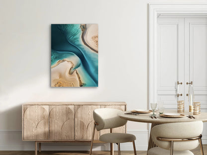 Textielkunstwerk met luchtfoto van water en zand in turquoise en beige, hangend boven houten kast in een licht interieur
