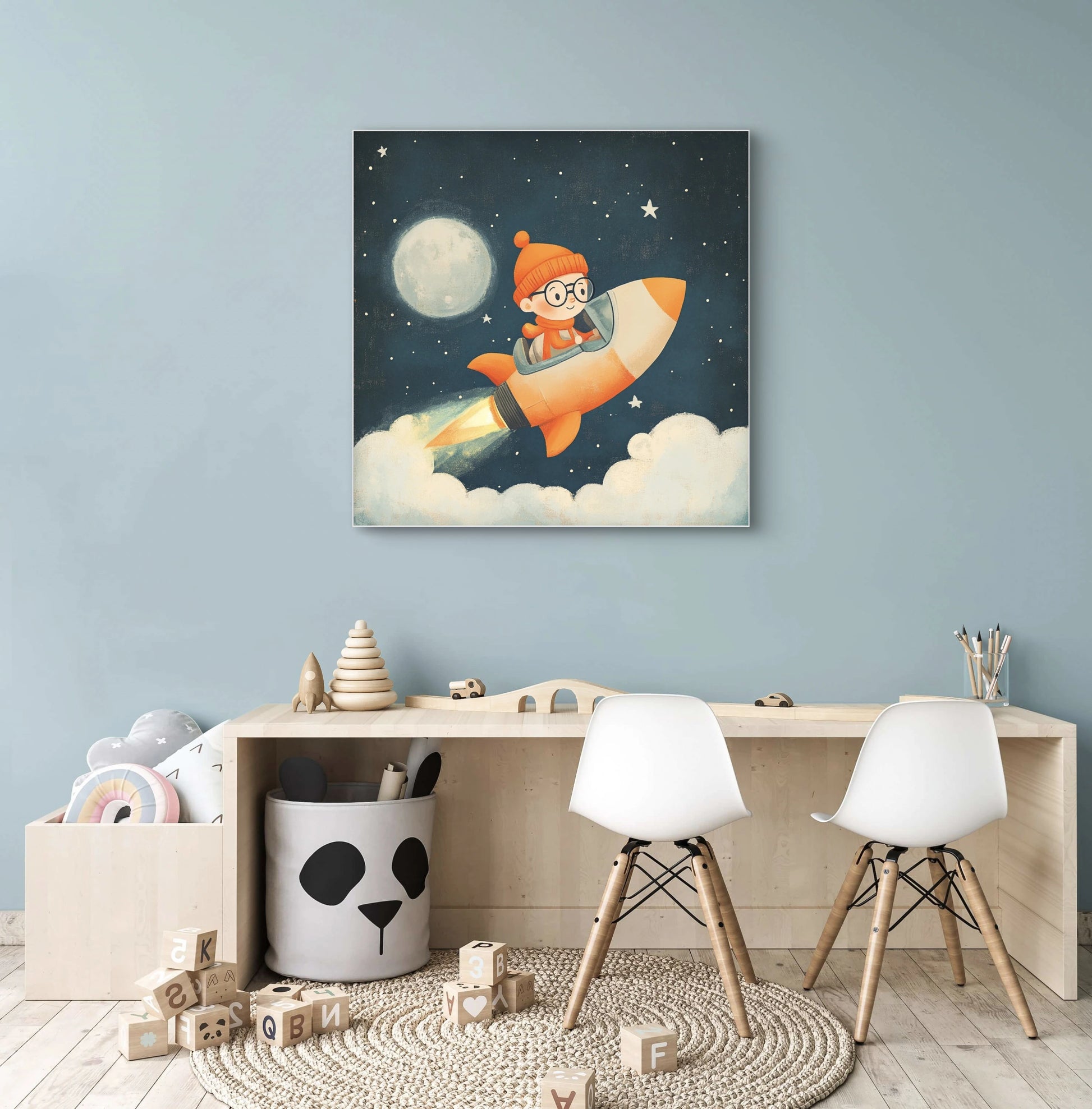 Mock-up van een kunstwerk met kind in raket aan een blauwe muur boven een houten kindertafel met stoeltjes en speelgoed.
