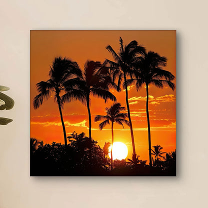 Detail van kunstwerk met zwarte palmbomen tegen een oranje lucht en laagstaande zon
