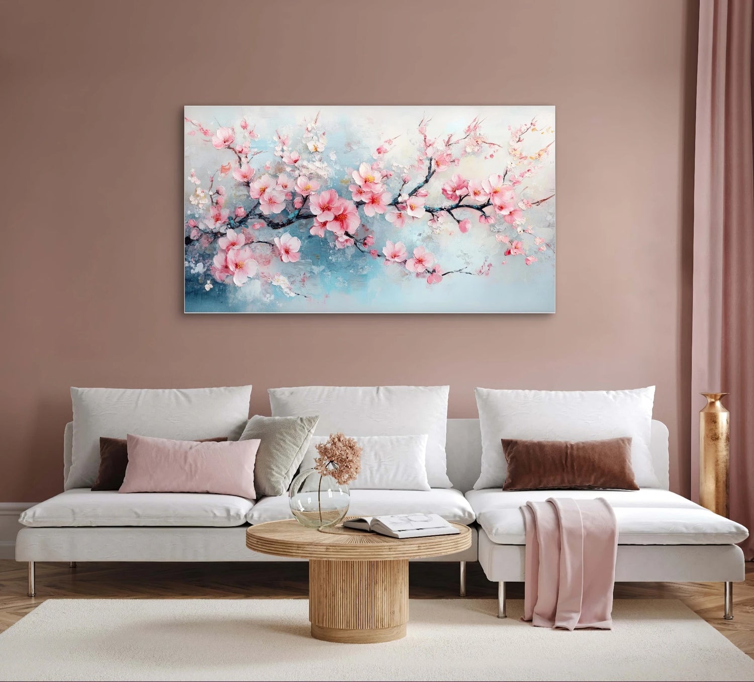 Textielkunstwerk met roze bloesems en blauwe achtergrond, hangend boven een witte bank in een warmroze woonkamer
