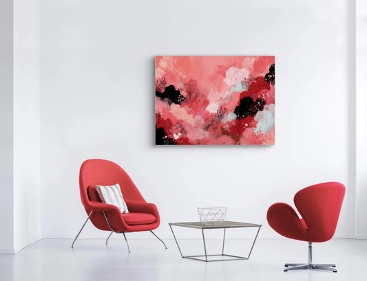 Abstract schilderij in rode, roze en zwarte tinten aan een witte muur boven rode stoelen
