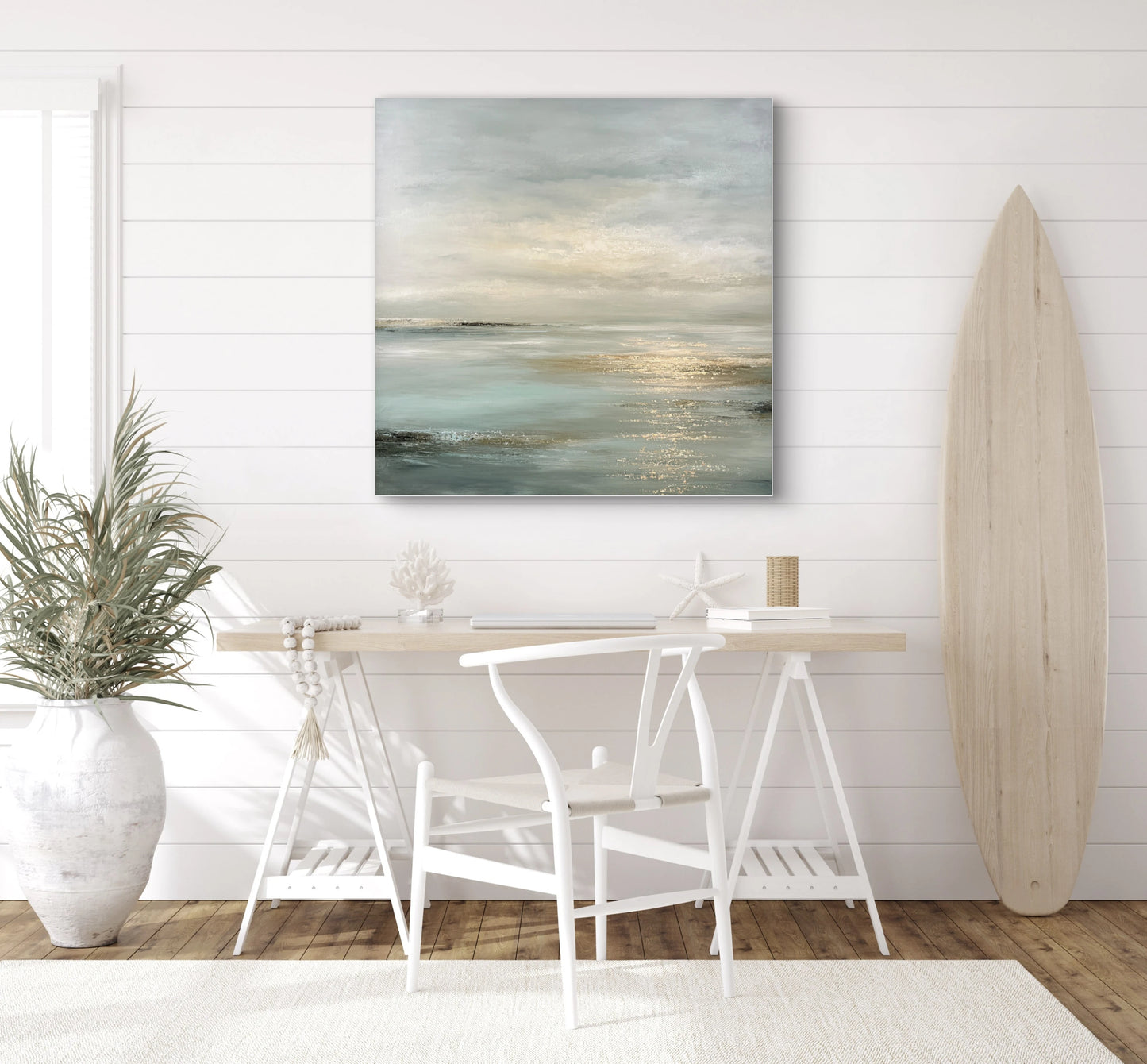 Abstract kunstwerk in blauwgrijs en goud tinten boven houten bureau in lichte kamer met surfplank
