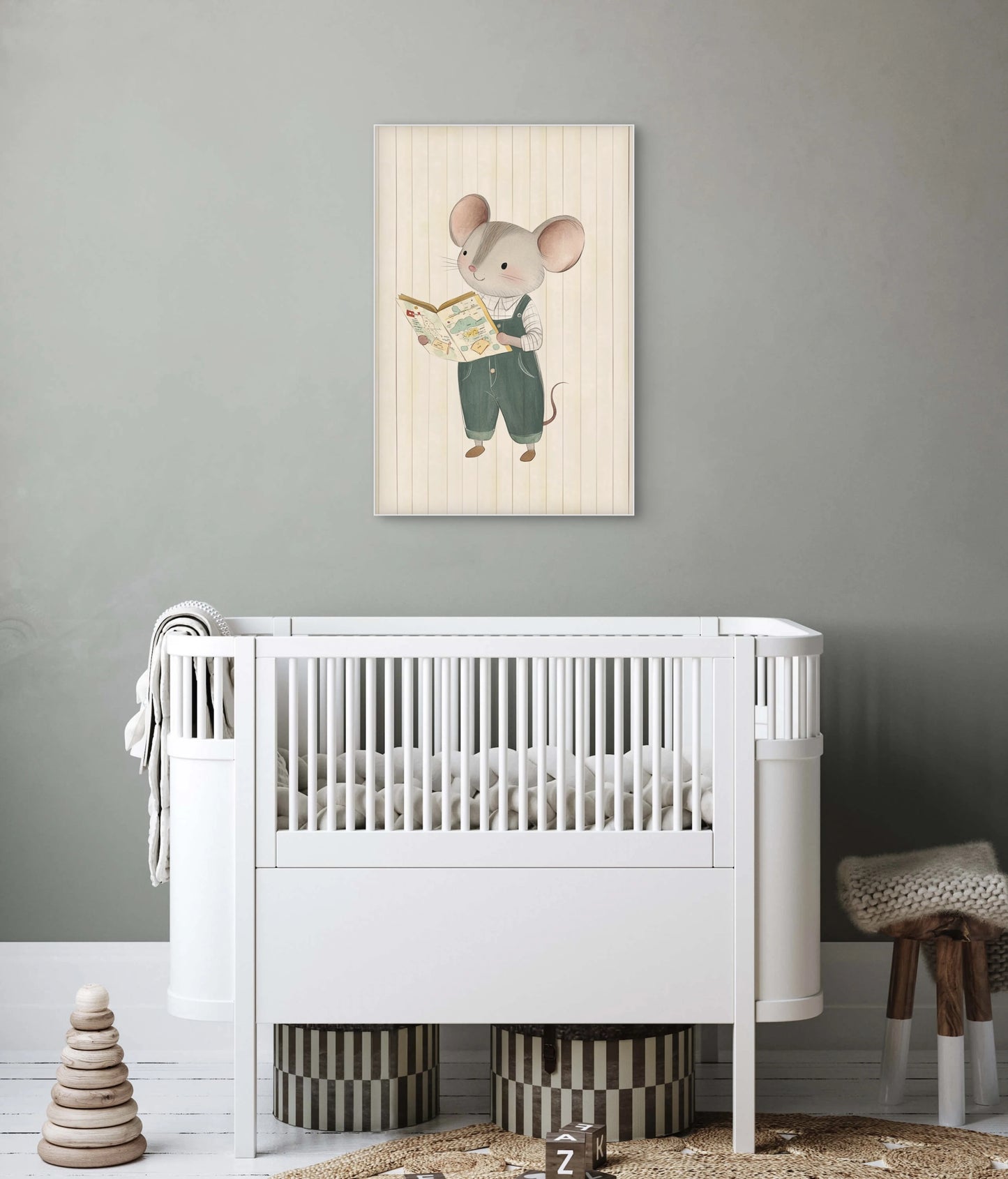 Mock-up van een babykamer met kunstwerk van een muis die een boek leest, aan een grijsgroene muur boven een wit babybedje.
