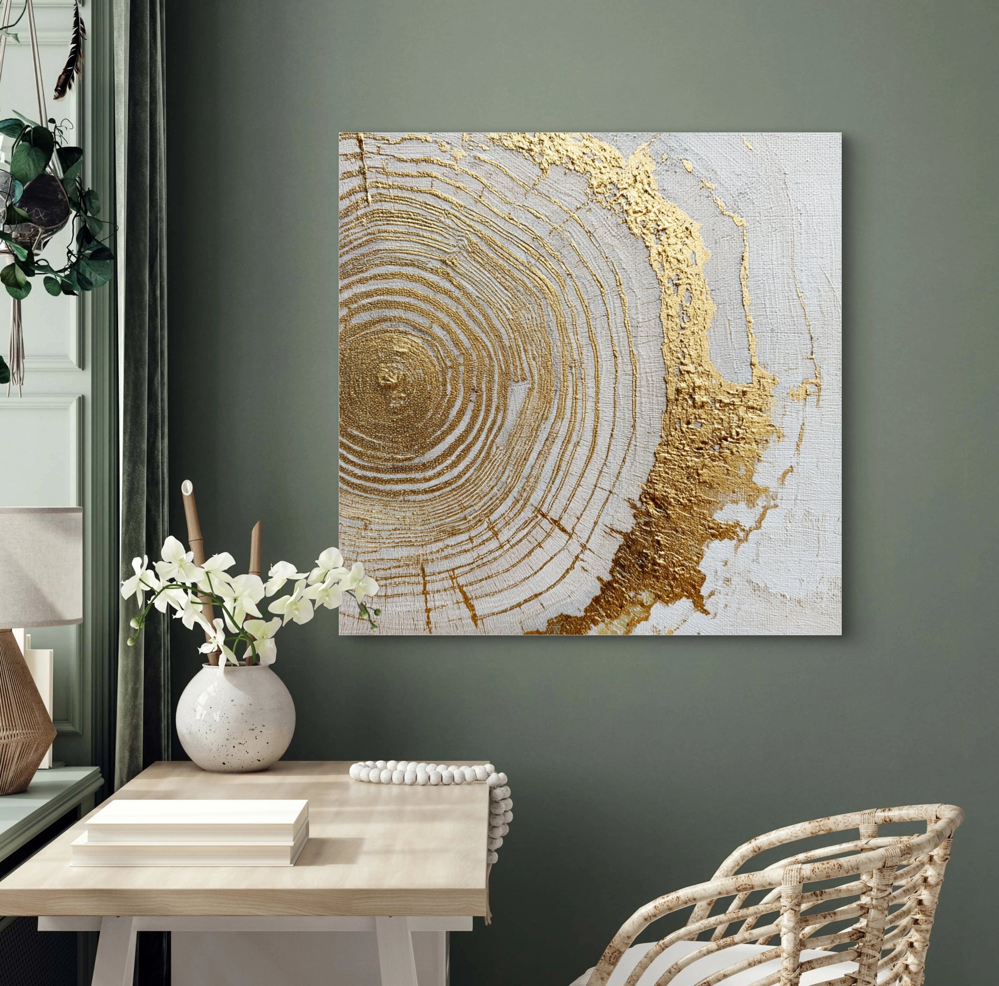 Textielkunstwerk Ringen van Goud boven een houten bureau met witte bloemen en groene muur.
