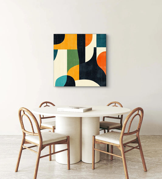 Modern geometrisch schilderij met grafische vlakken in warme en koele kleuren boven een ronde eettafel met houten stoelen
