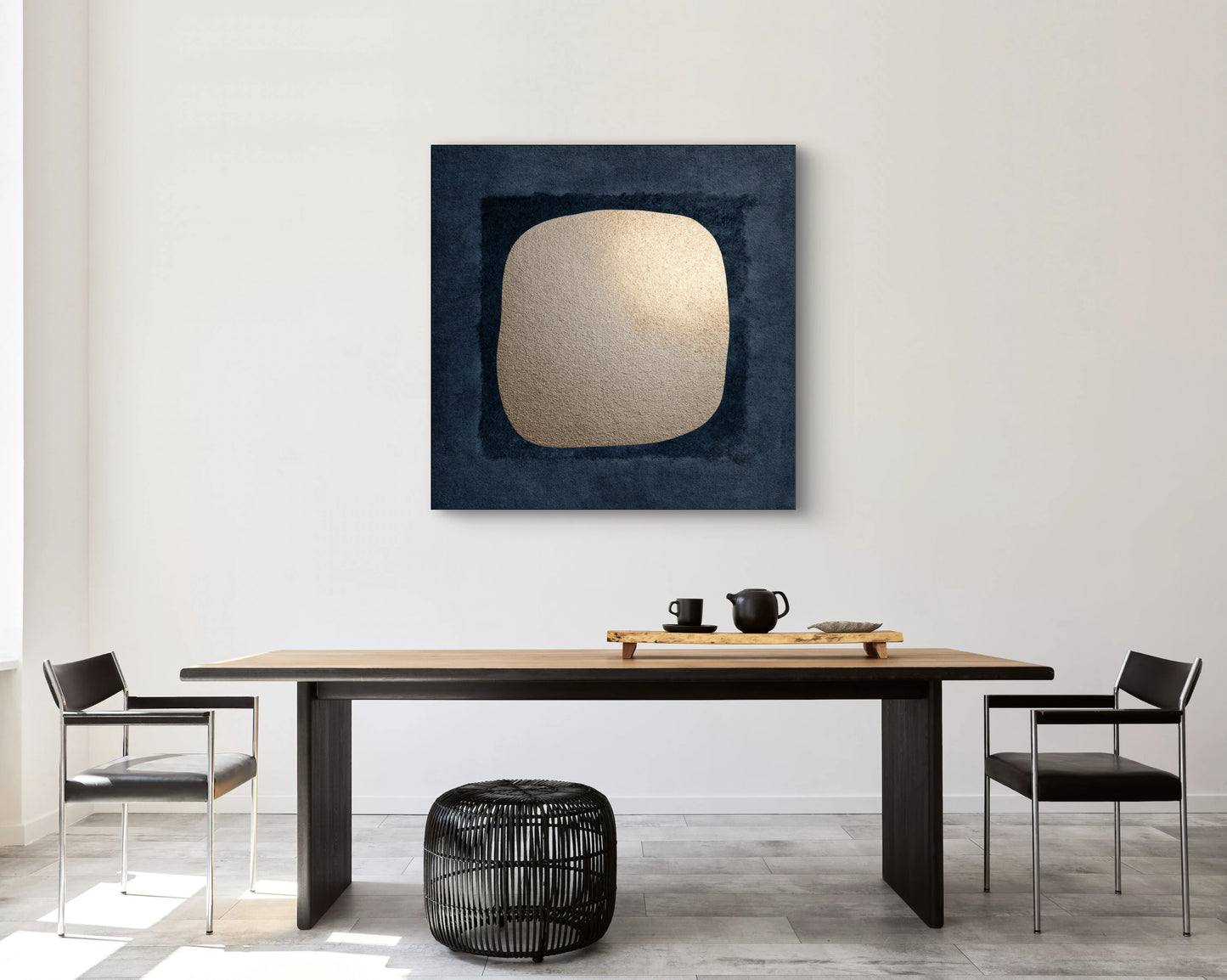 Kunstwerk Schaduw van Goud boven een houten eettafel met zwarte stoelen in een modern interieur.
