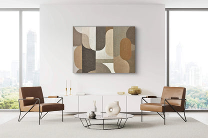 Textuurkunstwerk in aardetinten aan een witte muur boven een laag modern dressoir tussen twee leren stoelen in een licht interieur
