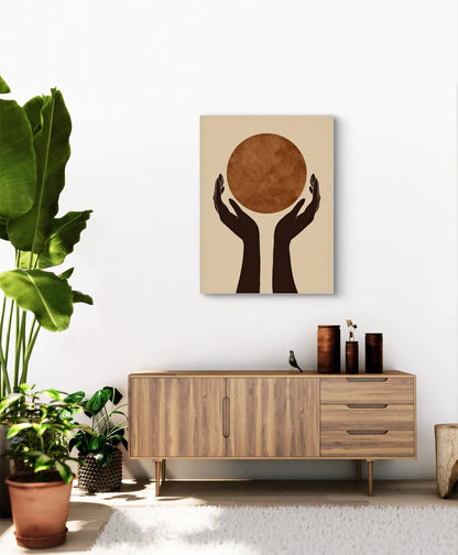 Abstract kunstwerk met twee zwarte handen die een roestbruine cirkel omhoog houden, aan een witte muur boven een houten kast met planten
