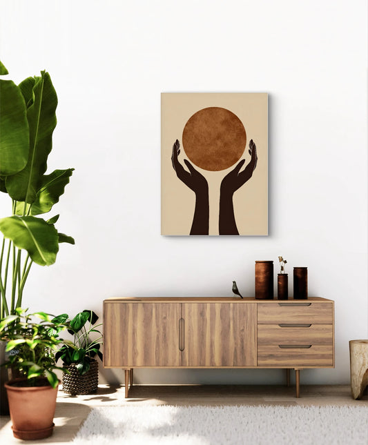 Abstract kunstwerk met twee zwarte handen die een roestbruine cirkel omhoog houden, aan een witte muur boven een houten kast met planten
