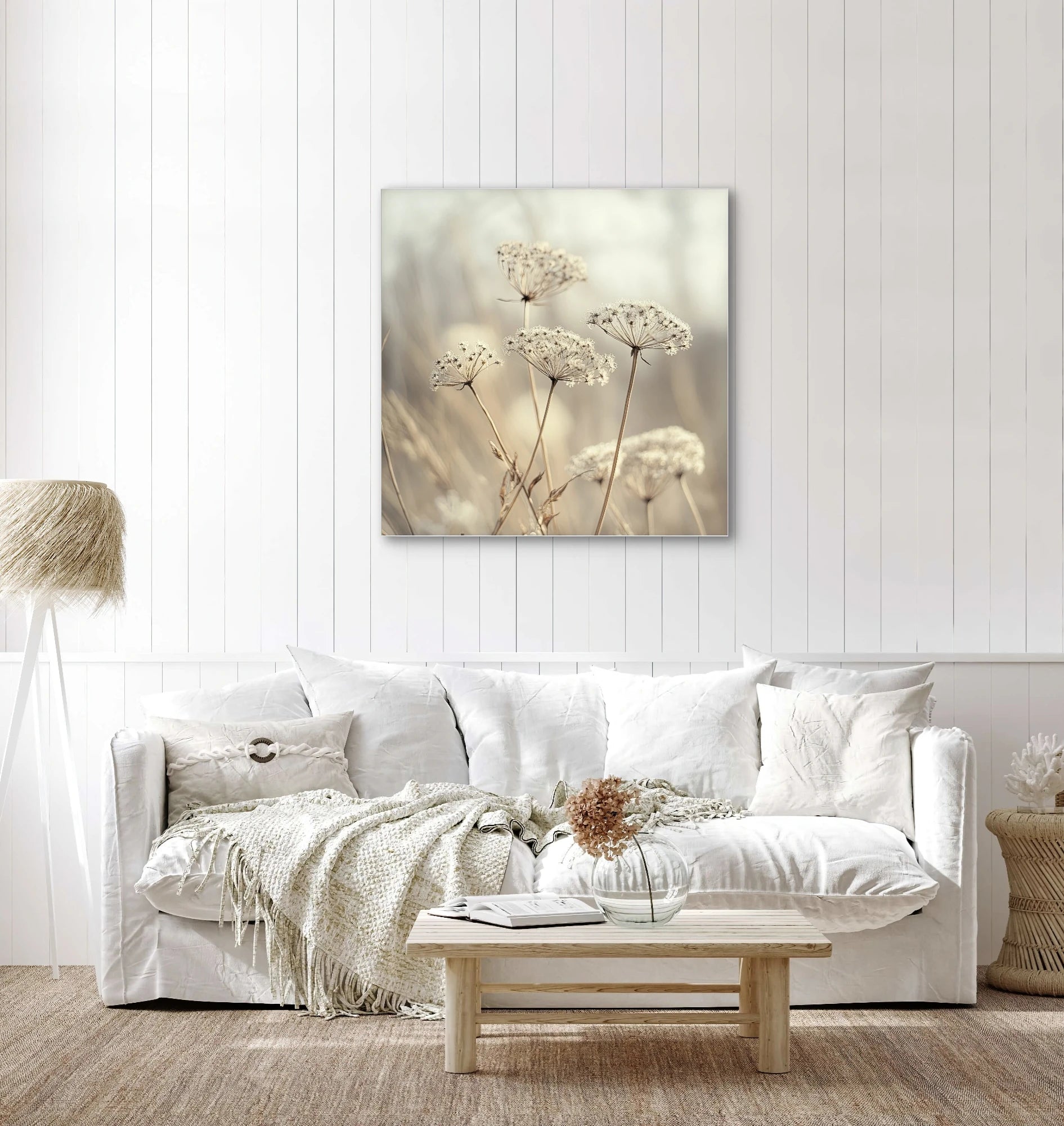 Textielkunstwerk met beige schermbloemen aan de muur in een wit interieur met licht houten accenten
