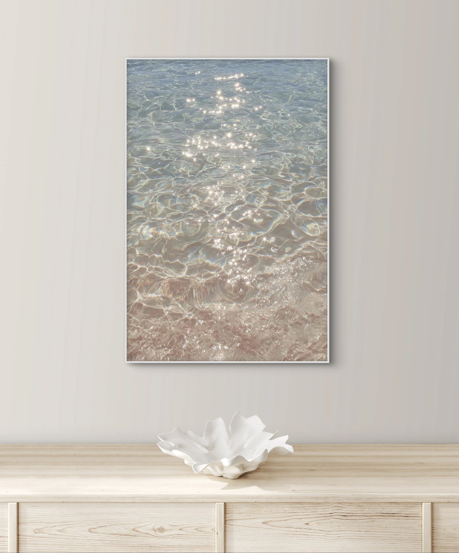 Fotografisch kunstwerk van glinsterend water aan de muur boven een houten dressoir met wit keramisch object
