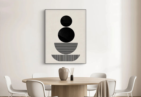 Textielkunstwerk met gestapelde zwarte vormen op beige achtergrond, hangend boven ronde houten tafel in een licht interieur
